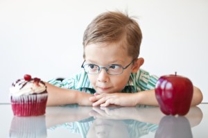 Little boy choosing between a cupcake and apple